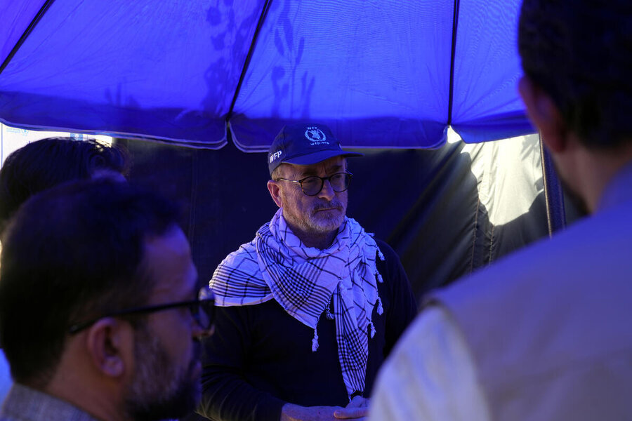 A white man with an Afghan shawl around his neck under a bit blue umbrella with male colleagues in Afghanistan