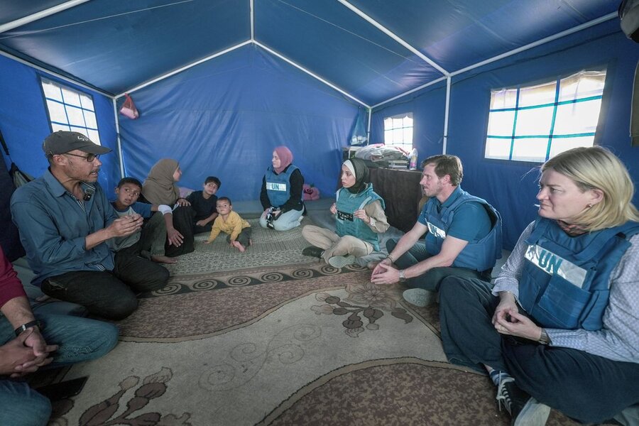 WFP staff in UN flak jackets sit cross-legged as they meet a family inside a humanitarian blue shelter in Gaza.