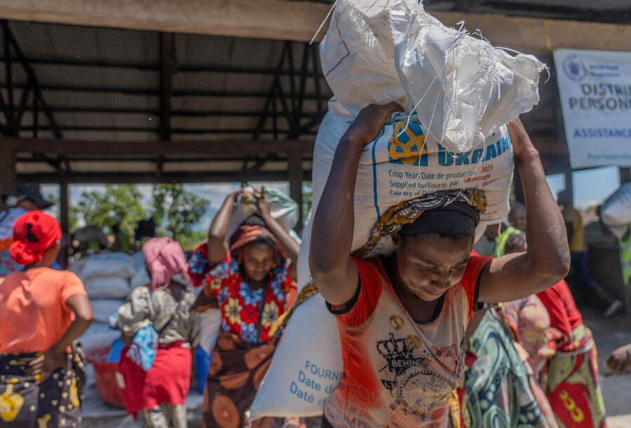 A woman carries away two WFP sacks of food assitance as others follow in DRC