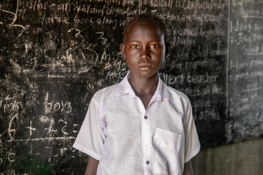A teenage school student stands in front of a blackboard in South Sudan