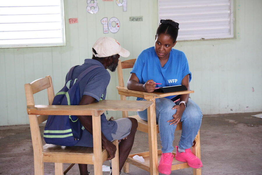 A woman in a blue WFP shirt takes information as she sits talking to a man