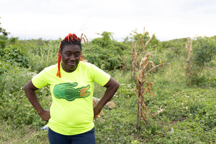 A woman in a bright yellow t-shirt and a huge crocodile logo smiles as she stands in a field