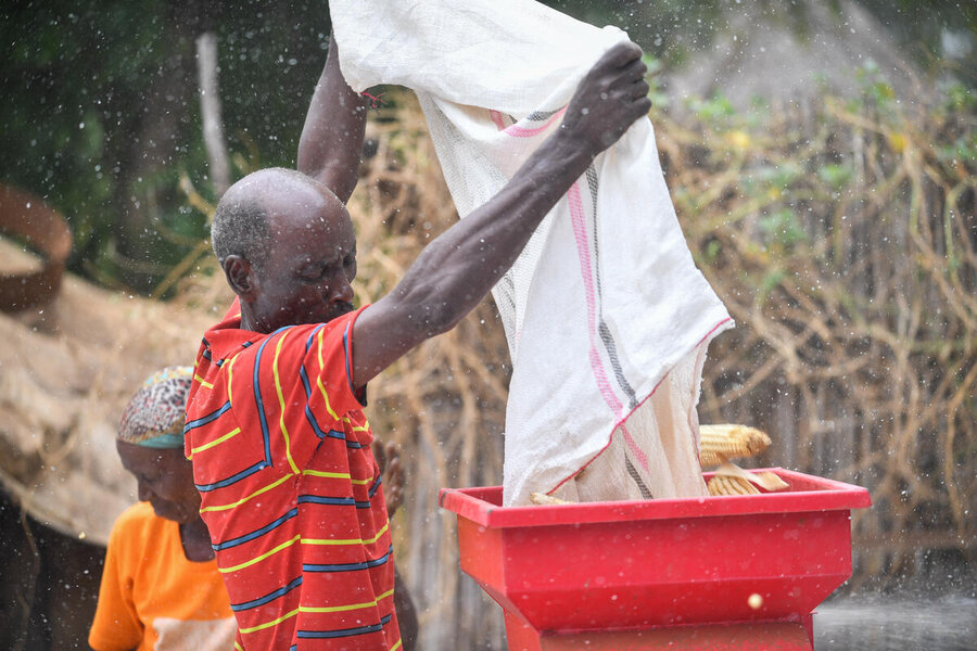Farmer Belete Abate pours maize from a burlap sack into a red threshing machine. Photo: WFP/Michael Tewelde
