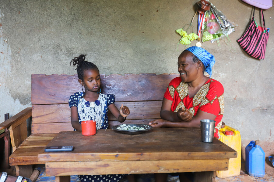 Marha Gonzar, wearing a blue headscarf and red dress, smiles as she watches her daughter Haimanot (in a blue-and-white dress) finish off a plate of rice. Photo: WFP/Michael Tewelde