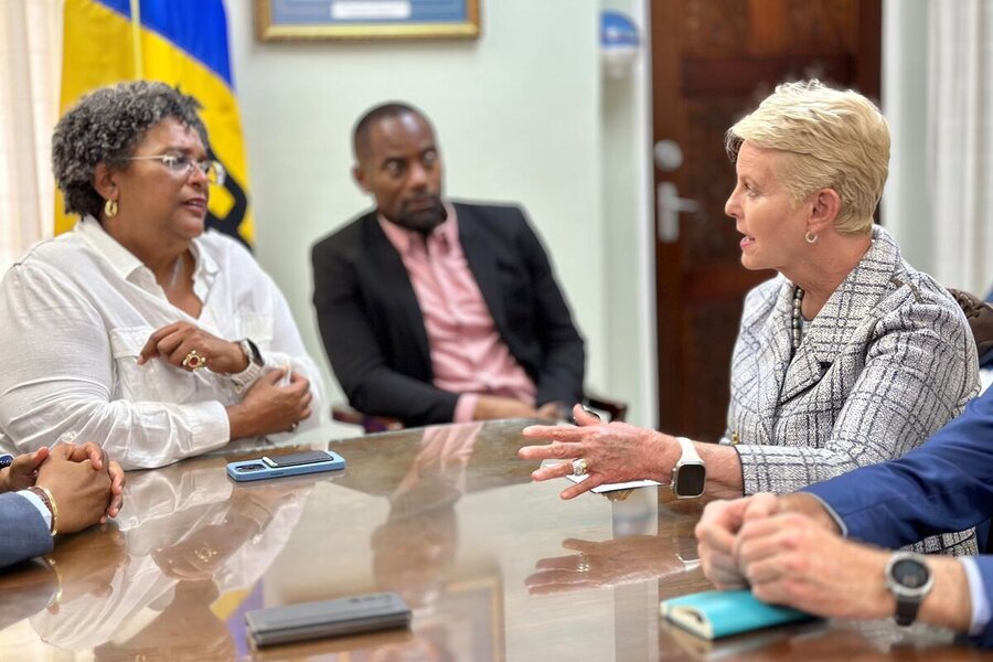 Prime Minister Mia Mottley of Barbados and Cindy McCain talk across an office desk with colleagues