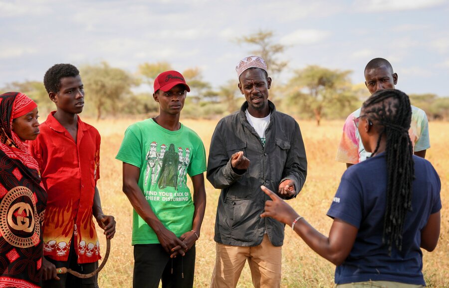 Five young farmer-herders stand in a golden field listening to a trainer explain farming techniques. Photo: WFP/Patrick Mwangi