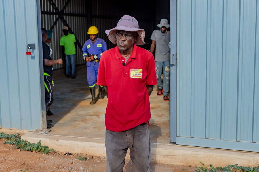 A man in a red shirt and grey hat stands outside a barn. Photo: WFP/Christopher Charamba 
