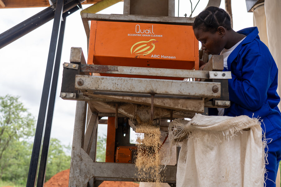 A woman in a dark blue jumpsuit feeds sesame grains through a red processor. Photo: WFP/Tatenda Macheka
