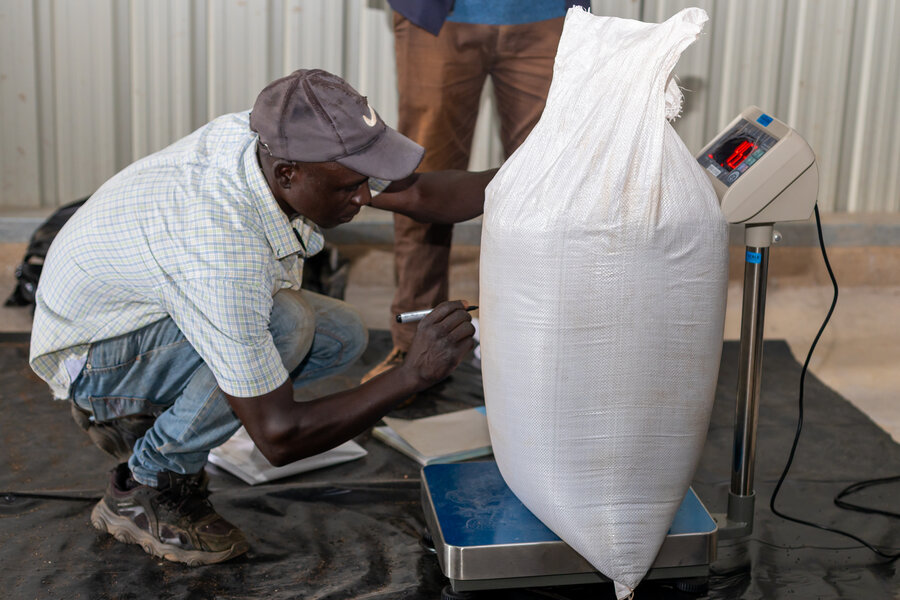 A worker in a white T-shirt and cap weighs a bag of sesame. Photo: WFP/Christopher Charamba