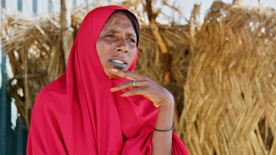 Woman in red gown wears a sorrowful expression as she sits next to a thatched wall in northeastern Nigeria. Photo: WFP/Arete/Nommiyid Chantu