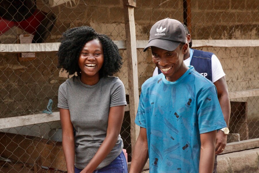 A smiling young woman in a grey shirt stands next to a smiling man in a blue shirt and cap. Photo: WFP/Nana Ivan de Amaral