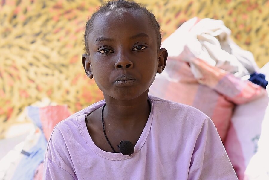 A little girl in a mauve T-shirt sits next to a pile of burlap bags