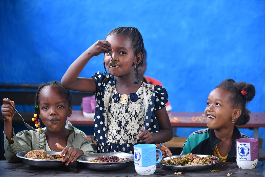 Three little girls in Ethiopia eat school meal, with two blue cups with the WFP logo. Photo: WFP/Michael Tewelde