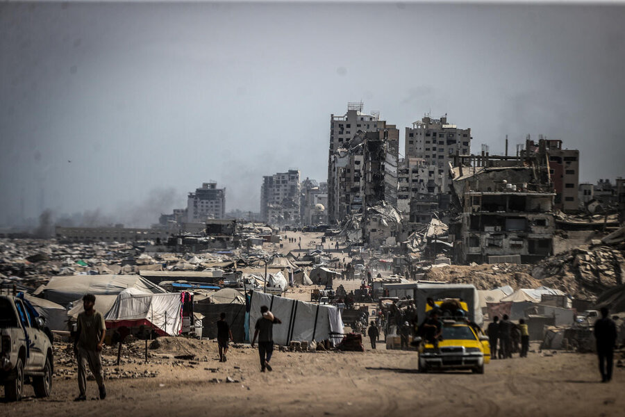 A sea of tents and destroyed buildings in the background, smokey air
