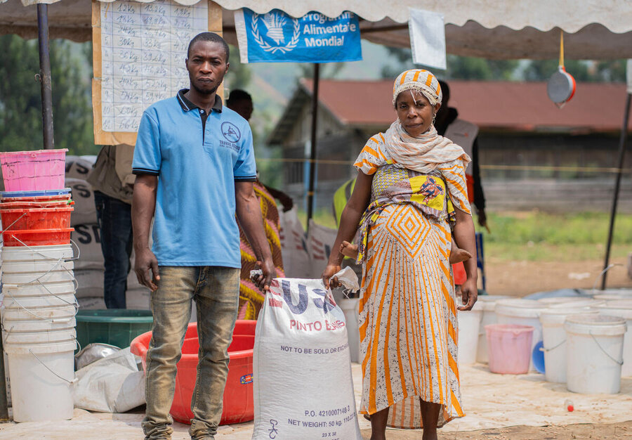 A man and woman with a sack of food assitance and a WFP sign in the background in DRC