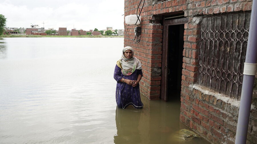 A woman knee deep in flood water outside her brick home, surrounding look like a lake