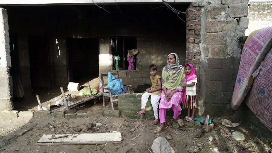 A woman with her two children sitting on a surface in her flood-destroyed home in Pakistan