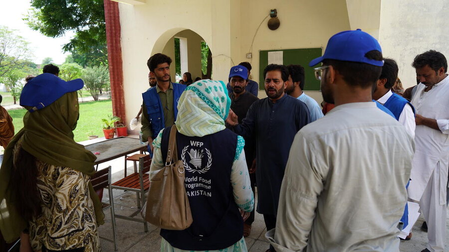 A woman wearing a blue WFP jacket, back to camera, speaks to male colleagues