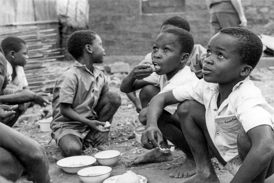 A black and white photos of boys aged around six squatting as they take food from bowls at a school