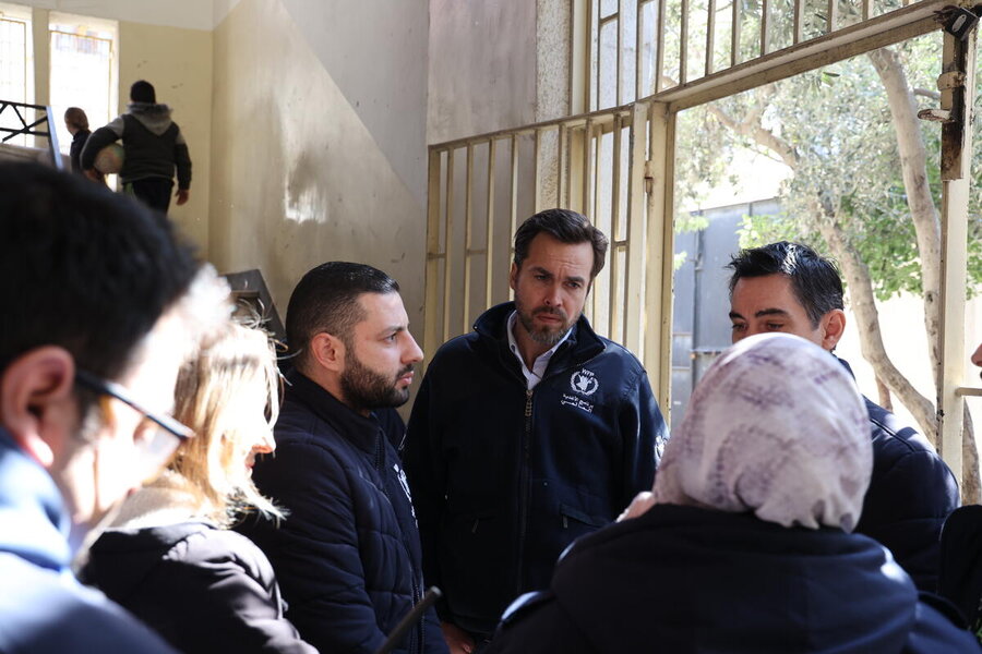 A man in a WFP jacket talks to people in the foyer of a school
