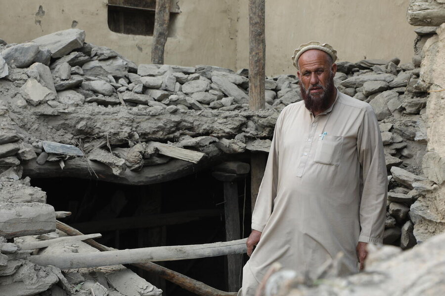 A man, wearing a cap and traditional Afghan gown, stands in front of a gaping hole that was his home before Afghanistan's quakes. Photo: WFP/Arete/Muktar Nikrawa