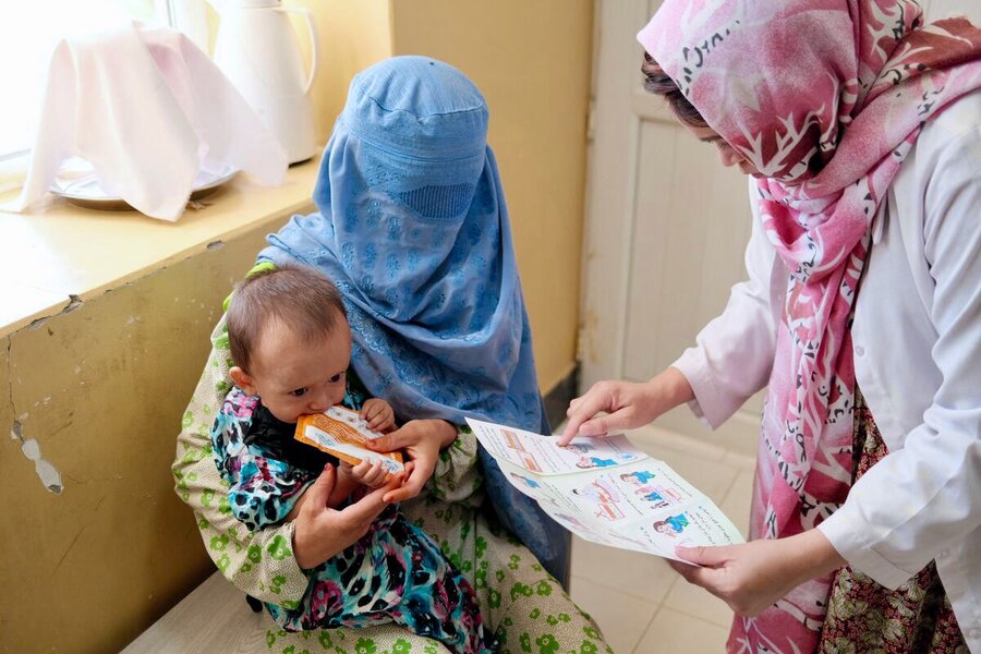 An Afghan woman in a blue burka cradles a child receiving WFP assistance as another woman holds a health leaflet. Photo: WFP/Anthea Piong