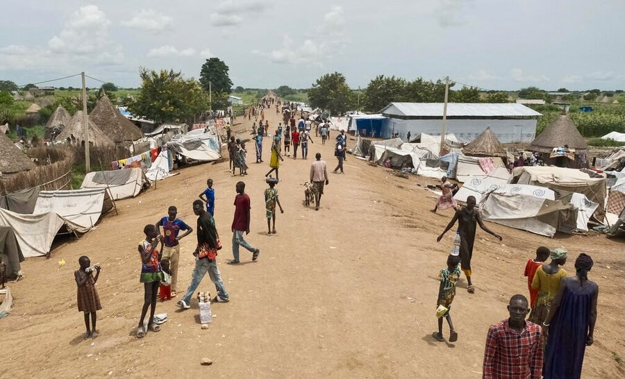Small white tents and thatched huts behind them line a dusty road where many people are walking. Photo: WFP/Michael Tewelde