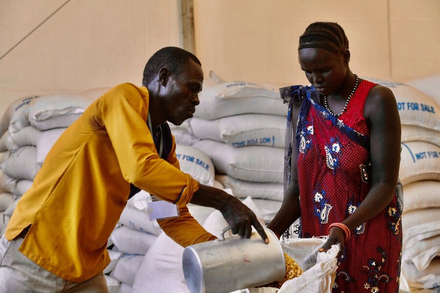 A man in a yellow shirt scoops grains into a big white bag held by a women in a red dress. Photo: WFP/Michael Tewelde
