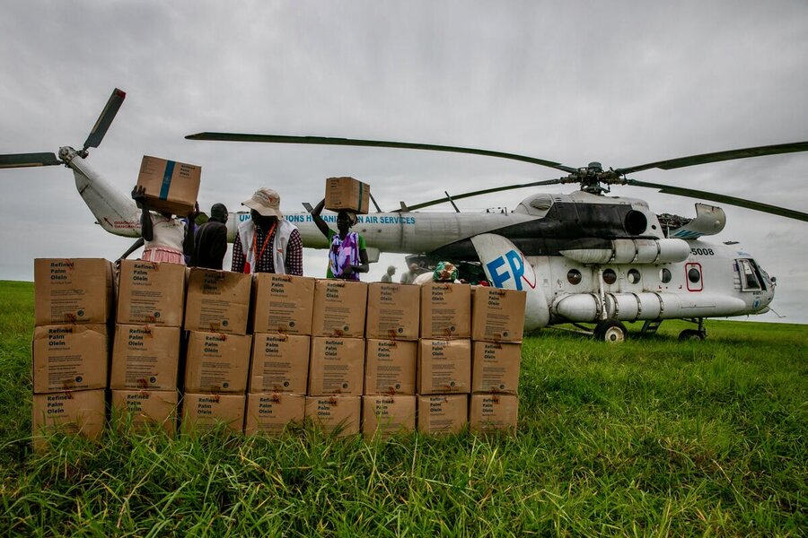 People carrying and looking at WFP boxes from an airdrop in South Sudan - with a WFP-managed UNHAS helicopter in the background. Photo: WFP/Eulalia Berlanga