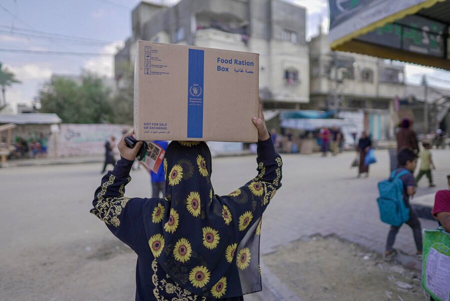 The back of a women in a colourful headscarf carrying a box of WFP food on her head. Photo: WFP/Jaber Badwan