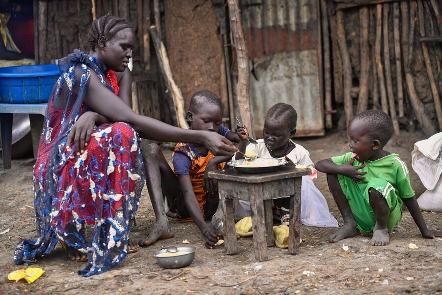 A woman feeds her three little children, who are gathered around a small and battered wooden table. Photo: WFP/Michael Tewelde