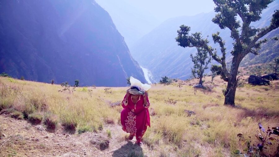 A woman in a traditional pink gown hikes up a mountainous path in Nepal carrying a bag of rice on her back. Photo: WFP