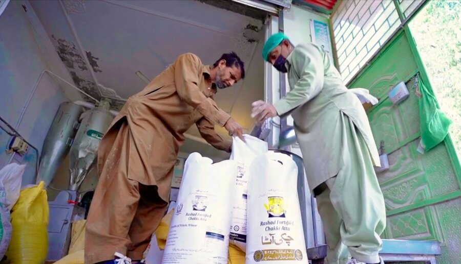 Two men lean over bags of fortified wheat. Photo: WFP