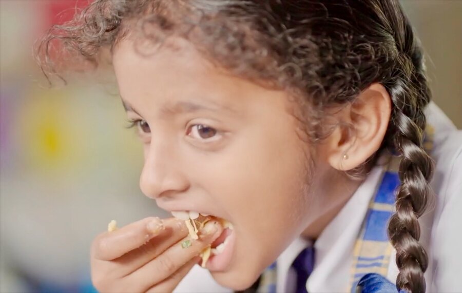 A smiling school girl in Bangladesh eats fortified food. Photo: WFP
