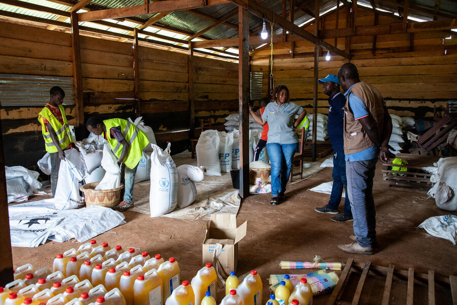 WFP staff check food aid supplies at a warehouse, including plastic jugs of vegetable oil and white bags of dried goods. Photo: WFP/Aurore Vinot