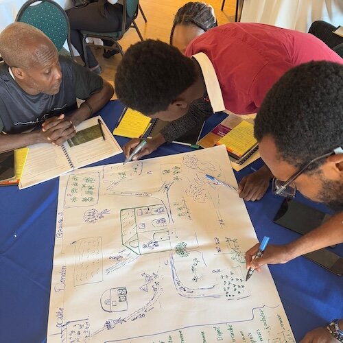 People gathered around a table drawing a detailed map on a large sheet of paper with notebooks and pens..