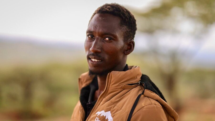 Closeup of a young man with a tan jacket backdropped by trees. Photo: WFP/Patrick Mwangi
