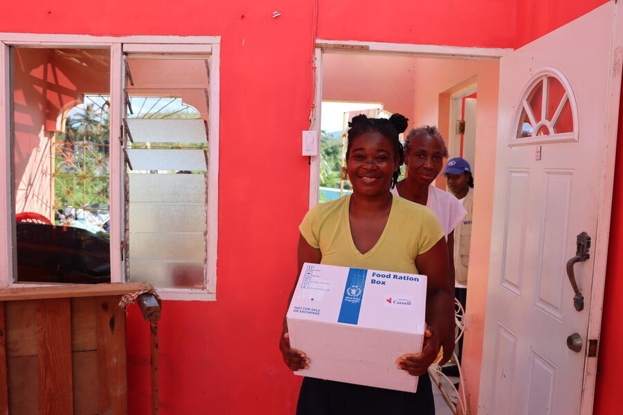 A woman carriies a WFP box into a red room with shattered windows