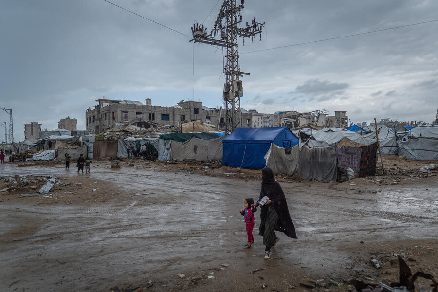 A woman guides a child through a raid-sodden street in Gaza
