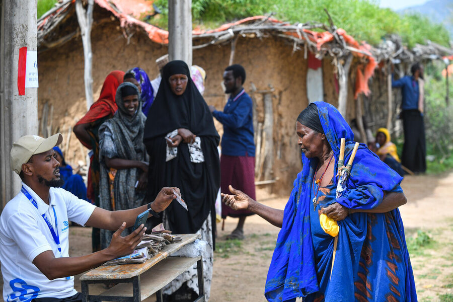 A man in white t-shirt and cap assists women lining up in a village in Ethiopia