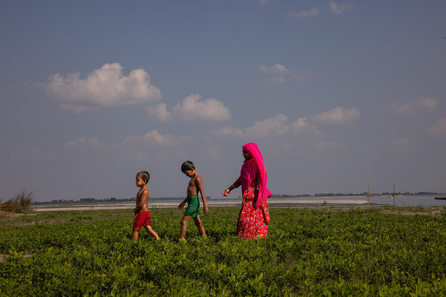 A woman and her two boys walk through a field, with a river in the background. Photo: WFP/Samantha Reinders