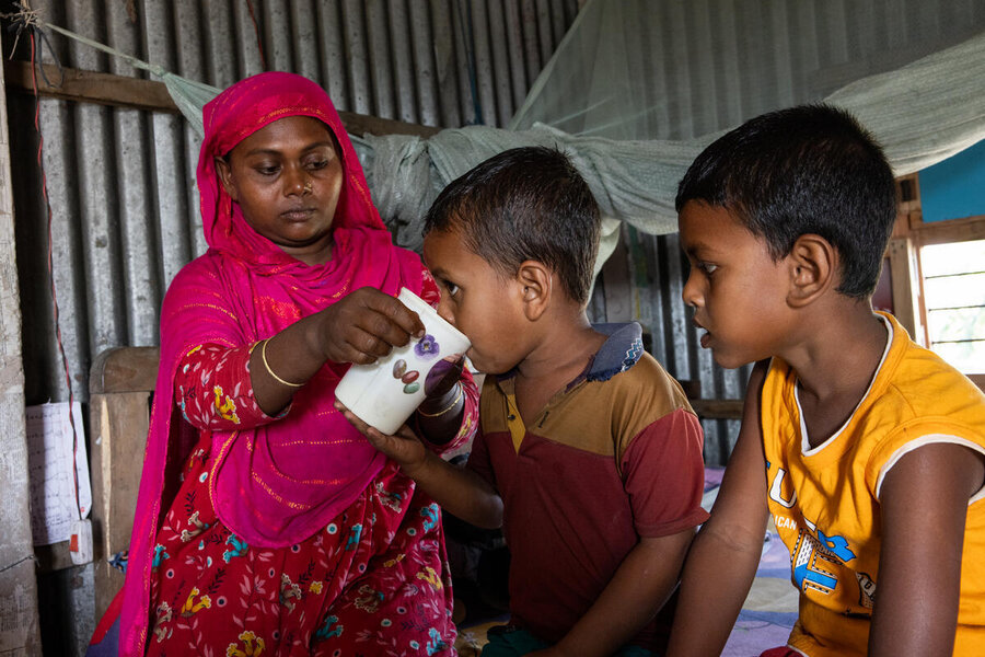 A woman in a pink headscarf and dress gives one of her two boys a drink. Photo: WFP/Samantha Reinders