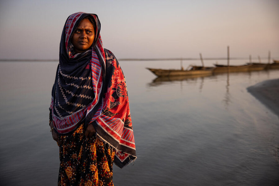 A woman in a colourful sari stands in front of a river, with a wooden canoe in the background. Photo: WFP/Samantha Reinders