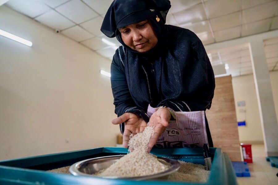 A woman in a black headscarf and robe sifts rice through her hands. Photo: WFP