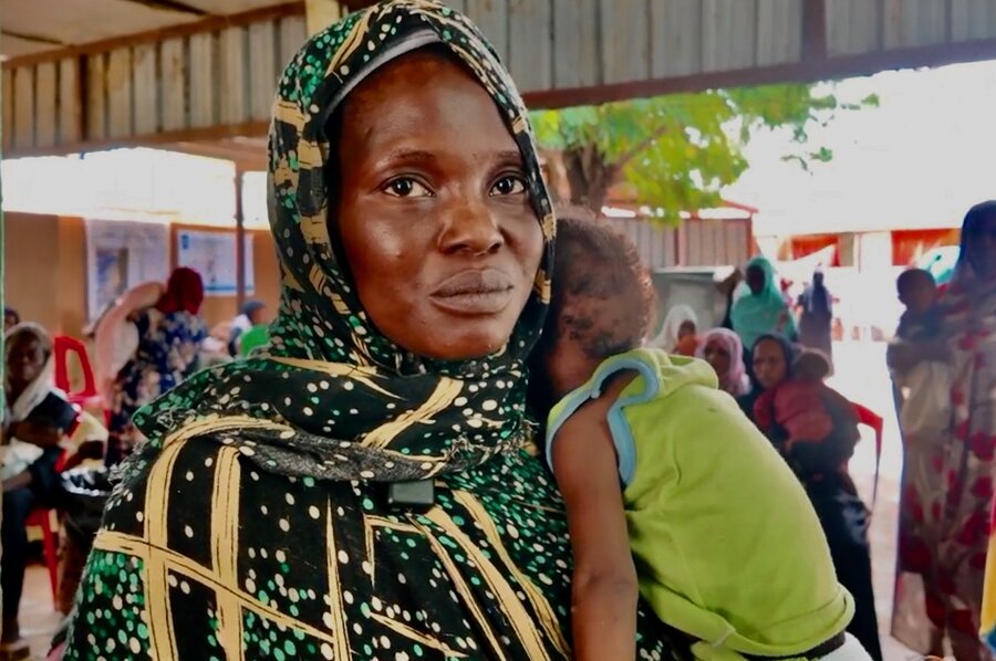 A woman in a green patterned headscarf with a sad expression holds a small child. Photo: WFP
