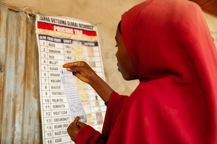 A young woman wearing a long red scarf checks a list of food commodities. Photo: WFP/Nommiyid Chantu