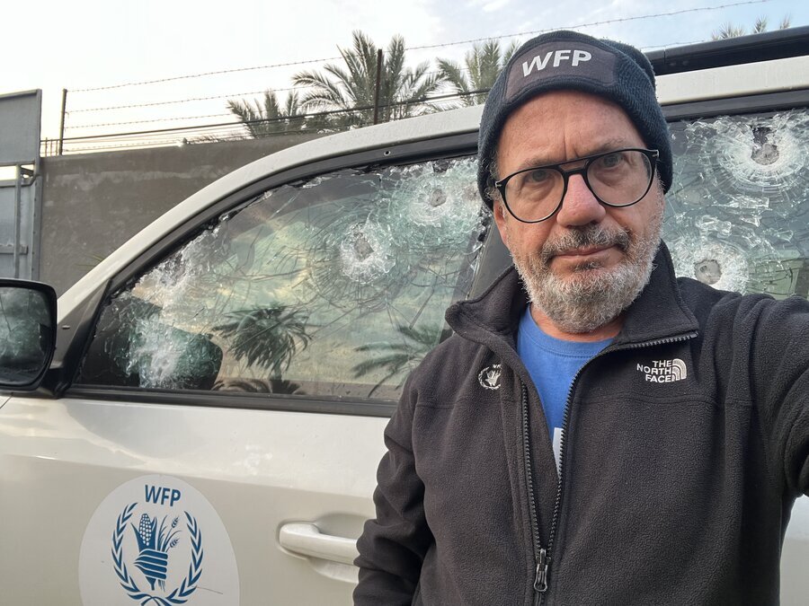 A man wearing a WFP bonnet stands in front of a bullet-riddled car. Photo: WFP/Jonathan Dumont