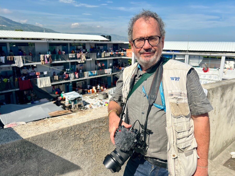 A man with a camera poses for a photo backdropped by a school that has become home for displaced people. Photo: WFP