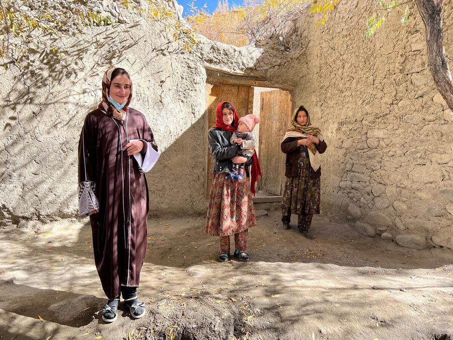 Three women stand in diagonal line in the middle of a clay roofless structure in Afghanistan