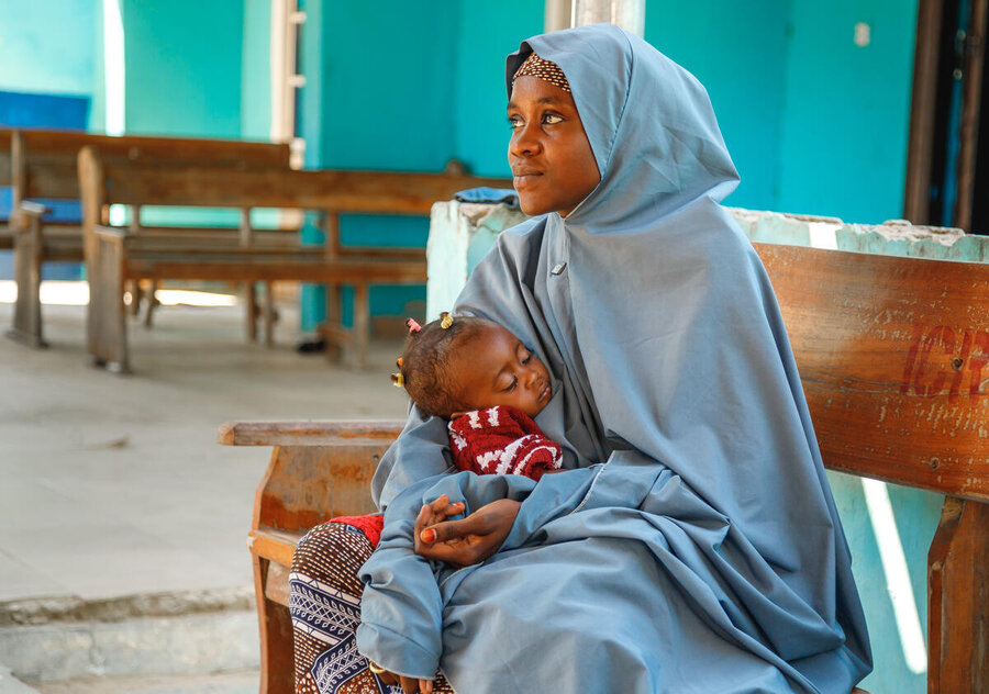 A young woman in a light blue veil and gown cradles a sleeping baby girl. Photo: WFP/Nommiyid Chantu